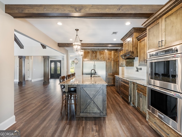 kitchen featuring dark wood-type flooring, light stone counters, stainless steel appliances, and ornate columns