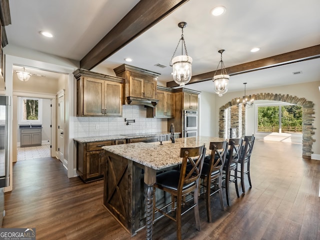 kitchen featuring a large island with sink, a healthy amount of sunlight, a notable chandelier, and dark hardwood / wood-style floors