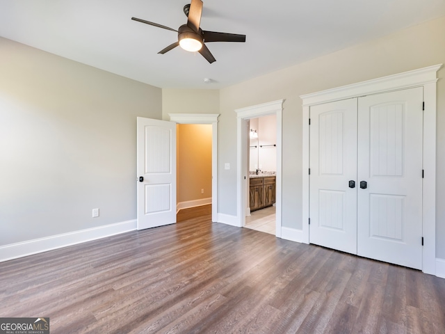 unfurnished bedroom featuring wood-type flooring, ensuite bathroom, ceiling fan, and a closet