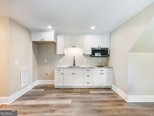 kitchen with light wood-type flooring, light stone counters, sink, and white cabinets