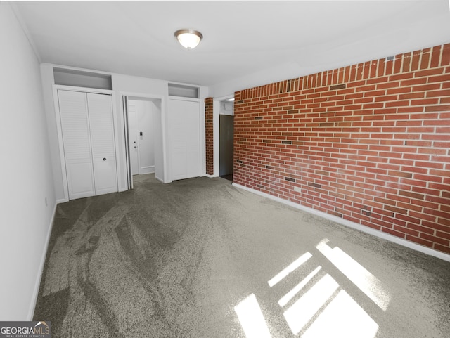 unfurnished bedroom featuring multiple closets, brick wall, and carpet flooring