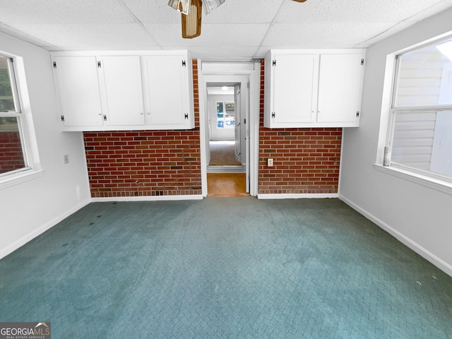 carpeted spare room with brick wall, a paneled ceiling, and ceiling fan