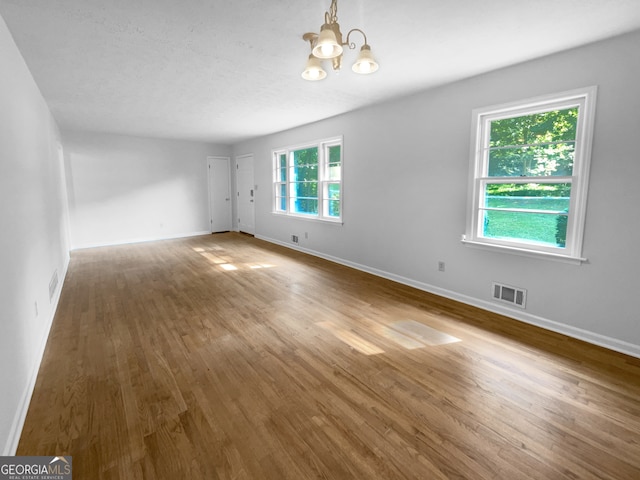 spare room with a healthy amount of sunlight, hardwood / wood-style floors, and a notable chandelier