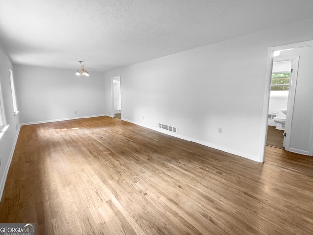 empty room featuring a textured ceiling, a notable chandelier, and hardwood / wood-style floors