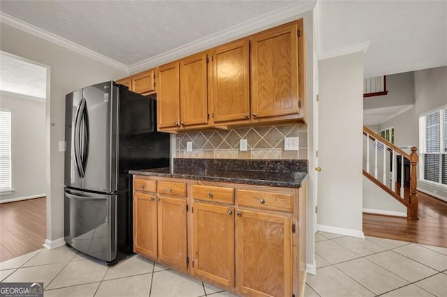 kitchen with stainless steel fridge, crown molding, decorative backsplash, light wood-type flooring, and dark stone counters