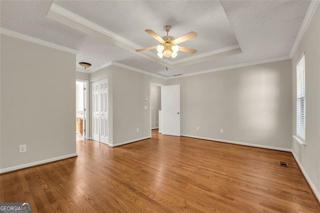 empty room with hardwood / wood-style floors, a tray ceiling, ceiling fan, ornamental molding, and a textured ceiling