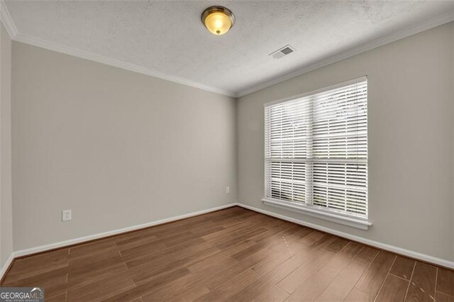 spare room with a textured ceiling, crown molding, and wood-type flooring