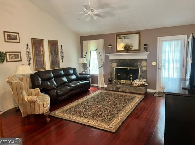 living room featuring a healthy amount of sunlight, dark hardwood / wood-style flooring, a stone fireplace, and vaulted ceiling