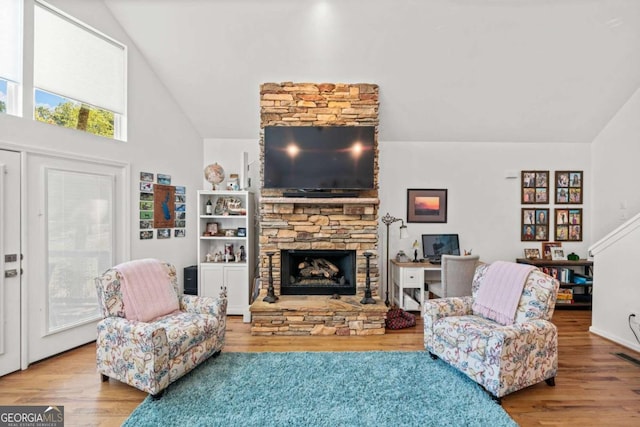 living room featuring a stone fireplace, high vaulted ceiling, and wood-type flooring