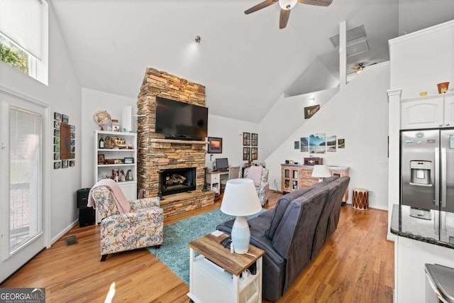 living room featuring ceiling fan, a fireplace, high vaulted ceiling, and light hardwood / wood-style floors