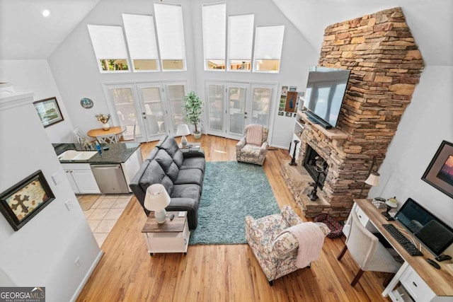 living room with french doors, sink, high vaulted ceiling, light hardwood / wood-style floors, and a fireplace