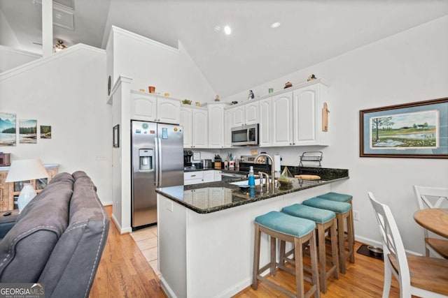 kitchen featuring dark stone counters, white cabinets, light wood-type flooring, appliances with stainless steel finishes, and kitchen peninsula