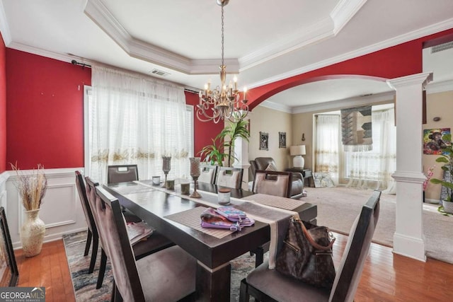 dining space with ornamental molding, hardwood / wood-style floors, a tray ceiling, and decorative columns