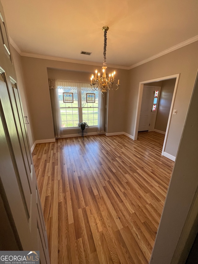 empty room featuring hardwood / wood-style floors, a chandelier, and crown molding