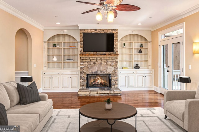 living room with hardwood / wood-style flooring, built in shelves, ornamental molding, ceiling fan, and a fireplace