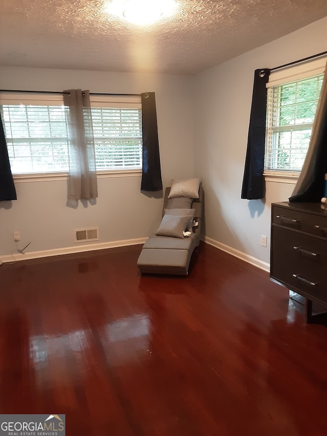 living area with a textured ceiling, plenty of natural light, and dark wood-type flooring