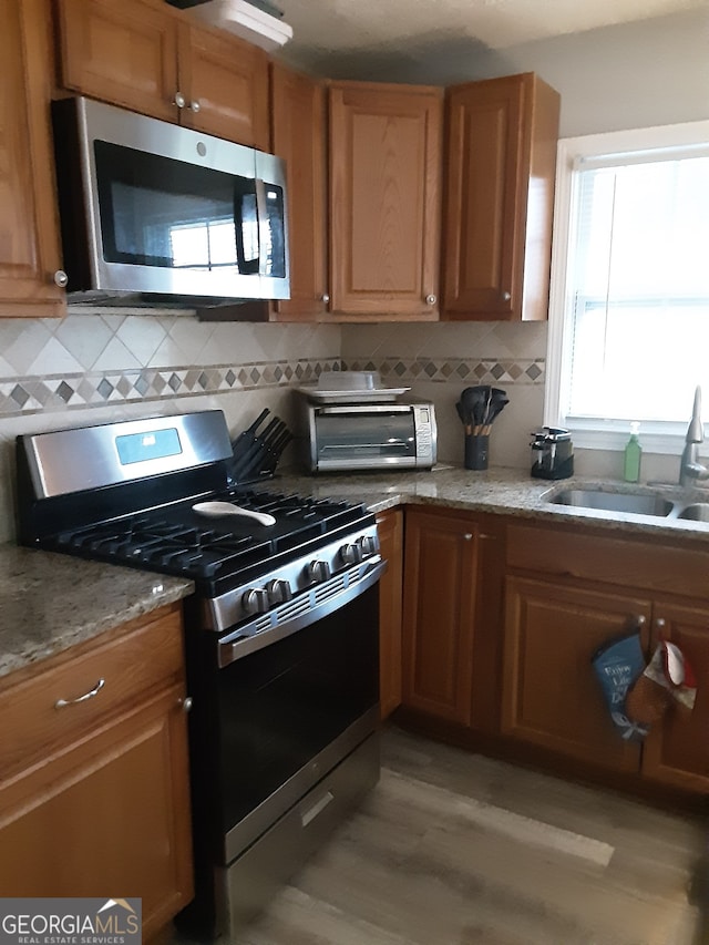 kitchen with stainless steel appliances, sink, light wood-type flooring, and tasteful backsplash