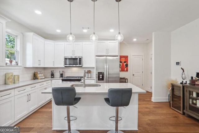 kitchen featuring hardwood / wood-style floors, appliances with stainless steel finishes, a center island with sink, and white cabinetry