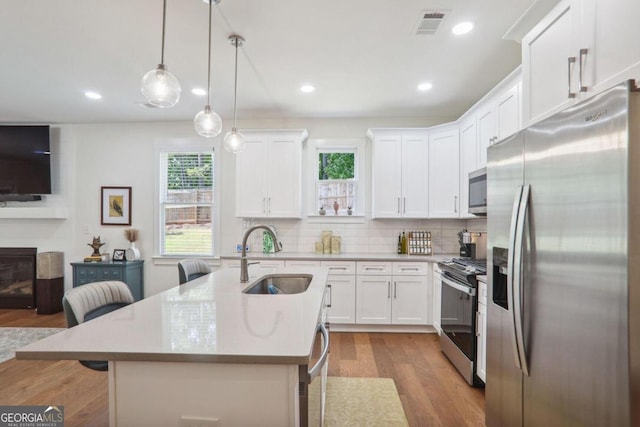 kitchen featuring appliances with stainless steel finishes, a wealth of natural light, a center island with sink, and sink