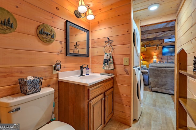 bathroom with toilet, vanity, wood walls, stacked washer / dryer, and hardwood / wood-style flooring