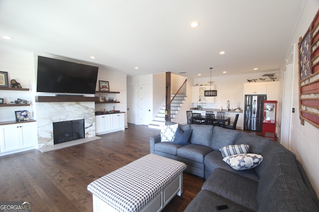 living room with a stone fireplace and dark wood-type flooring