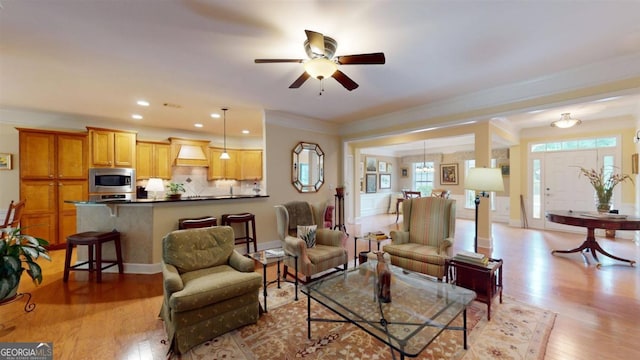 living room featuring crown molding, ceiling fan, and light wood-type flooring