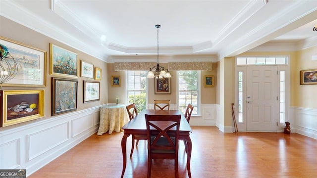 dining room with a raised ceiling, ornamental molding, a notable chandelier, and light hardwood / wood-style floors