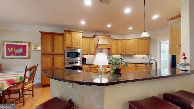 kitchen with light hardwood / wood-style flooring, decorative light fixtures, stainless steel appliances, kitchen peninsula, and custom range hood