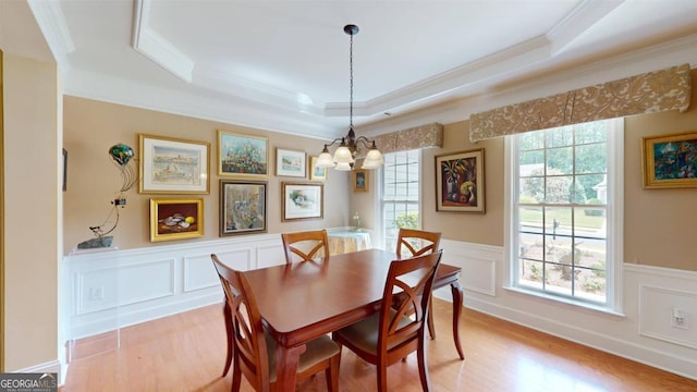 dining room with ornamental molding, light hardwood / wood-style flooring, a raised ceiling, and a chandelier