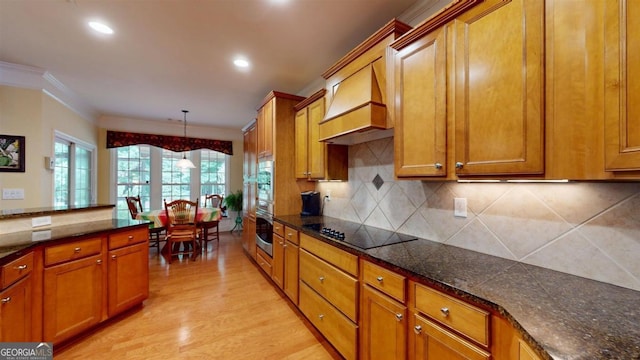 kitchen featuring hanging light fixtures, light wood-type flooring, premium range hood, black electric stovetop, and ornamental molding