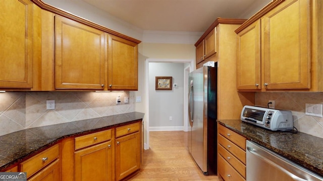 kitchen featuring appliances with stainless steel finishes, crown molding, decorative backsplash, dark stone countertops, and light wood-type flooring