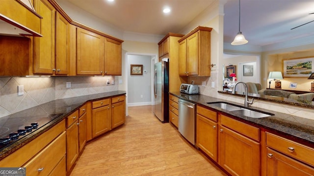 kitchen with decorative light fixtures, stainless steel appliances, sink, light wood-type flooring, and dark stone counters