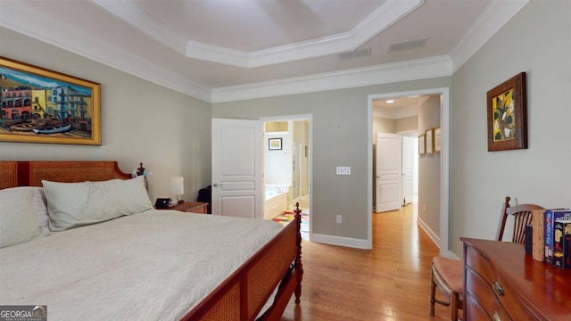 bedroom with light wood-type flooring, a raised ceiling, connected bathroom, and crown molding