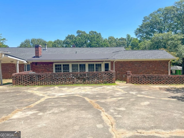 ranch-style house with roof with shingles, a chimney, and brick siding