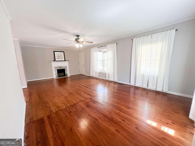 unfurnished living room with crown molding, a fireplace with flush hearth, a ceiling fan, wood finished floors, and baseboards