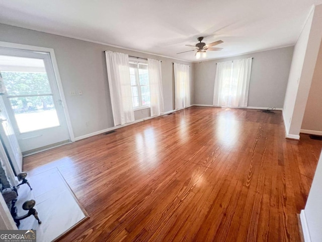 unfurnished living room with baseboards, visible vents, a ceiling fan, and wood finished floors