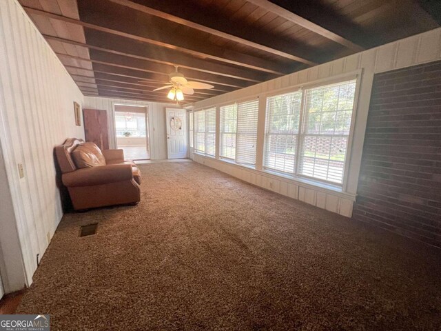 living area featuring a healthy amount of sunlight, ceiling fan, beam ceiling, and carpet flooring