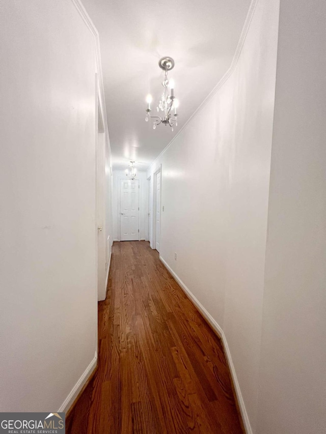 hallway with wood-type flooring, an inviting chandelier, and ornamental molding