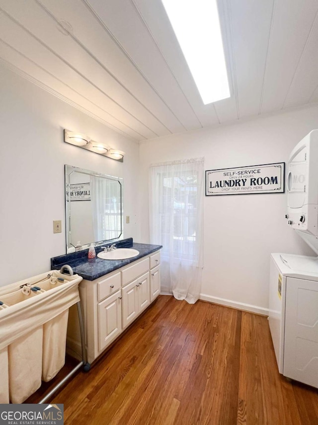 bathroom featuring a skylight, a sink, stacked washing maching and dryer, and wood finished floors