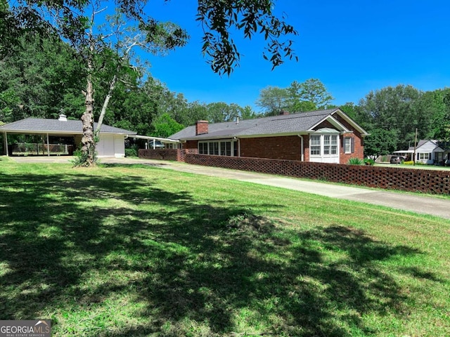 view of side of property featuring a chimney, brick siding, a yard, and driveway