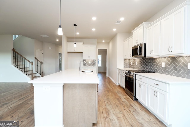 kitchen featuring pendant lighting, sink, appliances with stainless steel finishes, an island with sink, and white cabinets