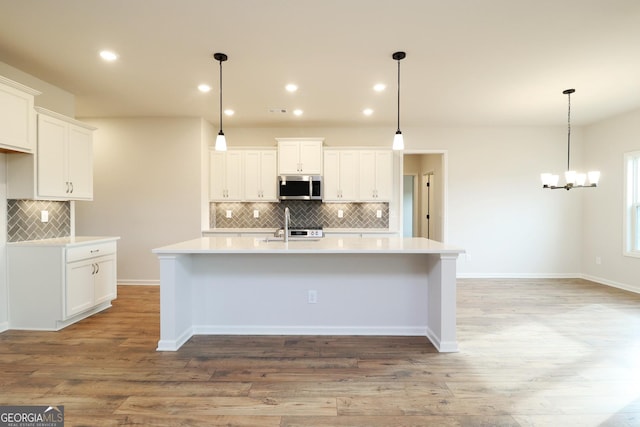 kitchen with decorative light fixtures, a center island with sink, and white cabinets