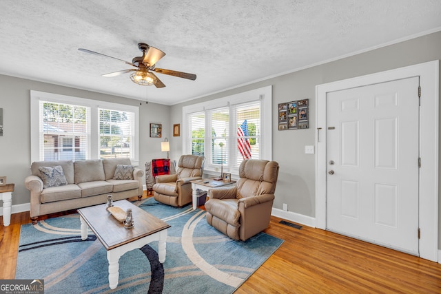 living room with light wood-type flooring, ceiling fan, crown molding, and a textured ceiling