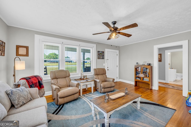 living room featuring light wood-type flooring, ceiling fan, ornamental molding, and a textured ceiling