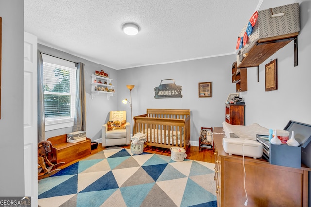 bedroom featuring a textured ceiling, light hardwood / wood-style floors, and a crib