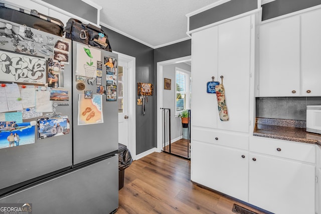 kitchen featuring a textured ceiling, crown molding, stainless steel refrigerator, hardwood / wood-style flooring, and white cabinetry