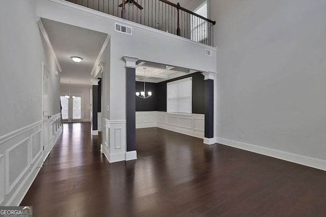 unfurnished living room featuring dark hardwood / wood-style flooring, decorative columns, and a notable chandelier