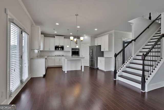 kitchen with appliances with stainless steel finishes, dark wood-type flooring, white cabinets, a kitchen island, and hanging light fixtures