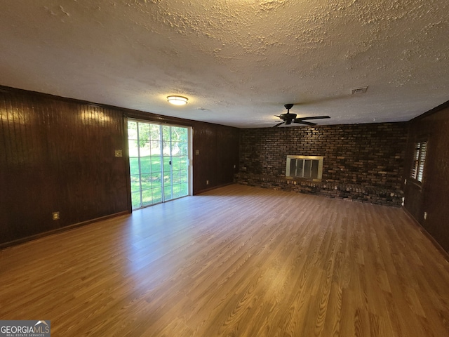 unfurnished living room with a textured ceiling, wood walls, hardwood / wood-style floors, and a fireplace