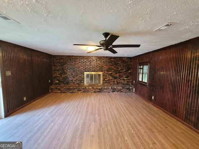 unfurnished living room featuring a fireplace, wooden walls, a textured ceiling, ceiling fan, and light hardwood / wood-style floors